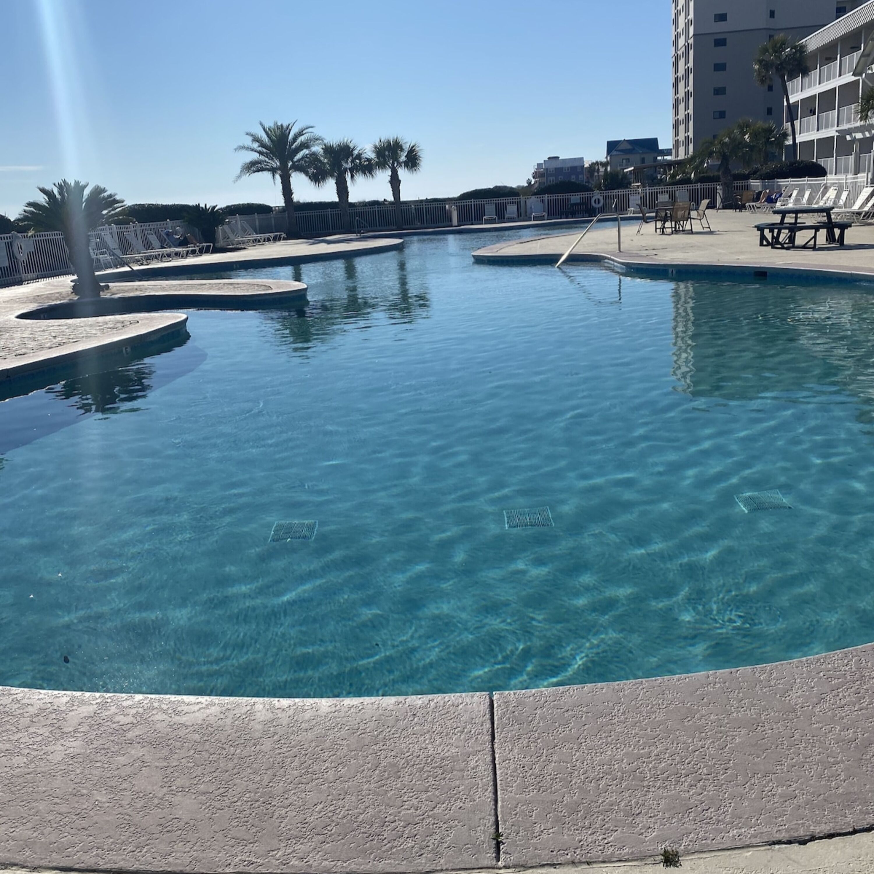 A clear blue pool with lounge chairs and palm trees.