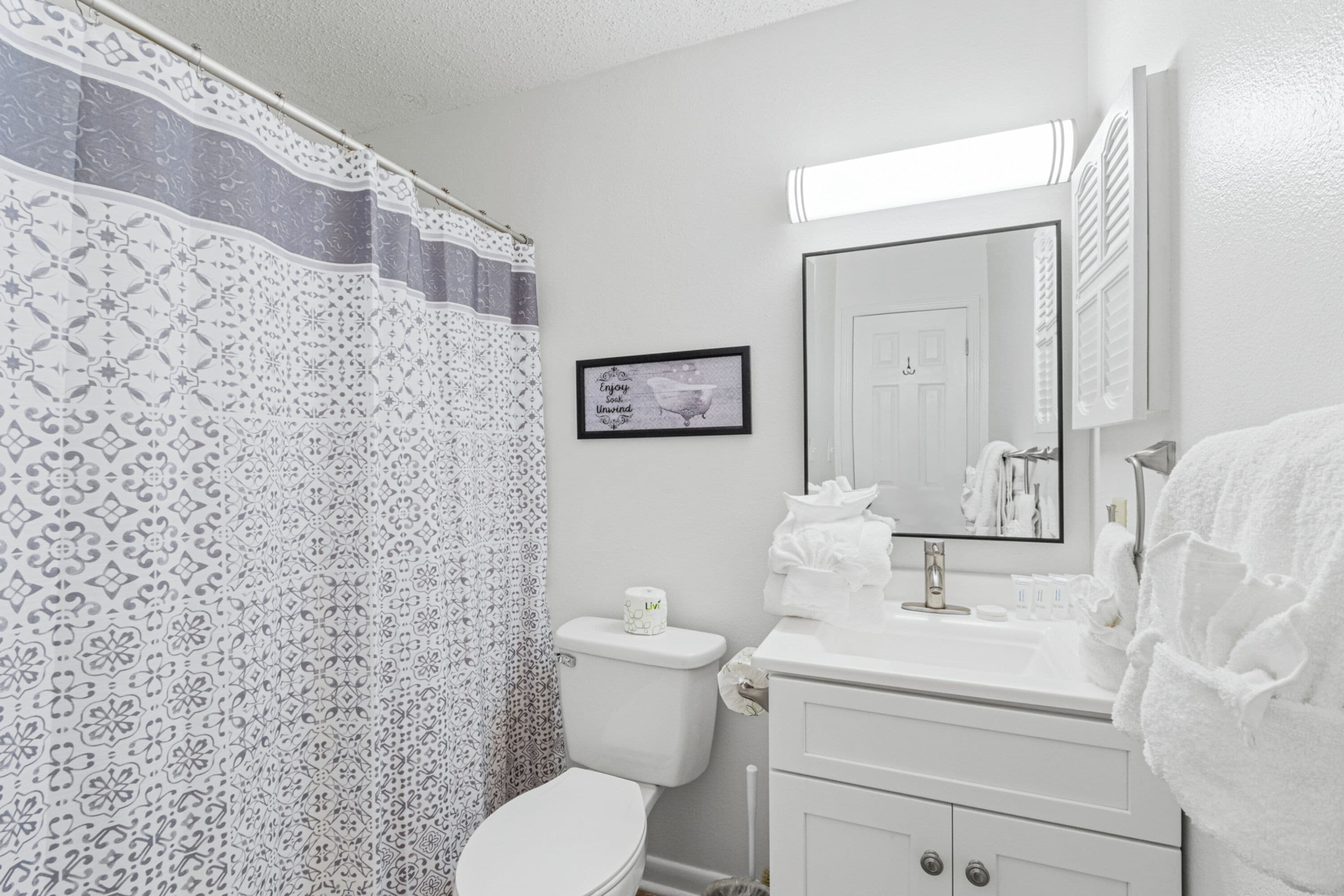A bathroom with a patterned shower curtain, a toilet, a sink with a mirror, and a towel rack.