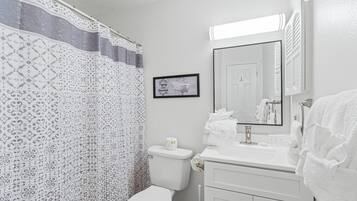 A bathroom with a patterned shower curtain, a toilet, a sink with a mirror, and a towel rack.