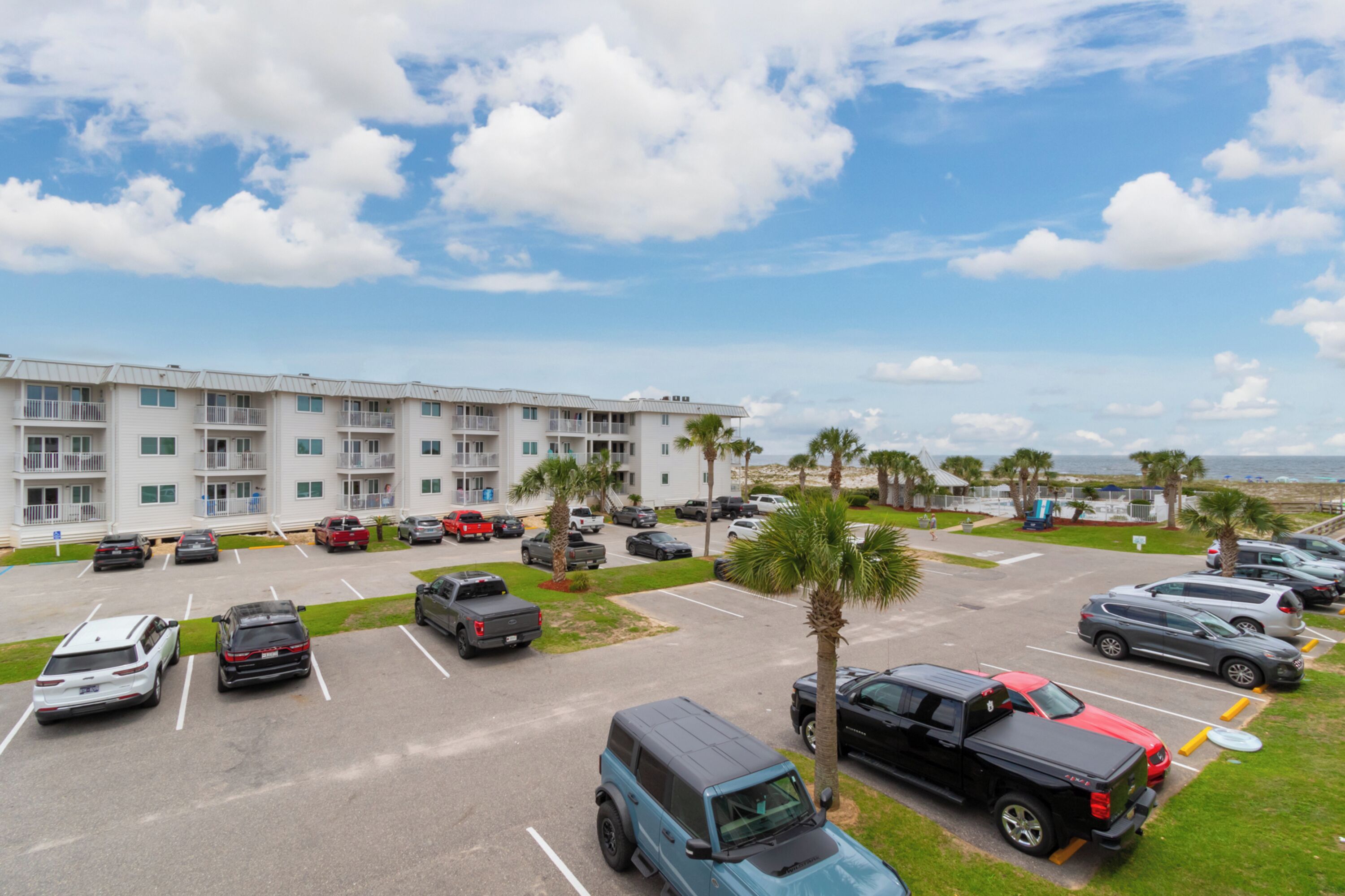 A parking lot with various vehicles, a multi-story building with balconies, and palm trees.