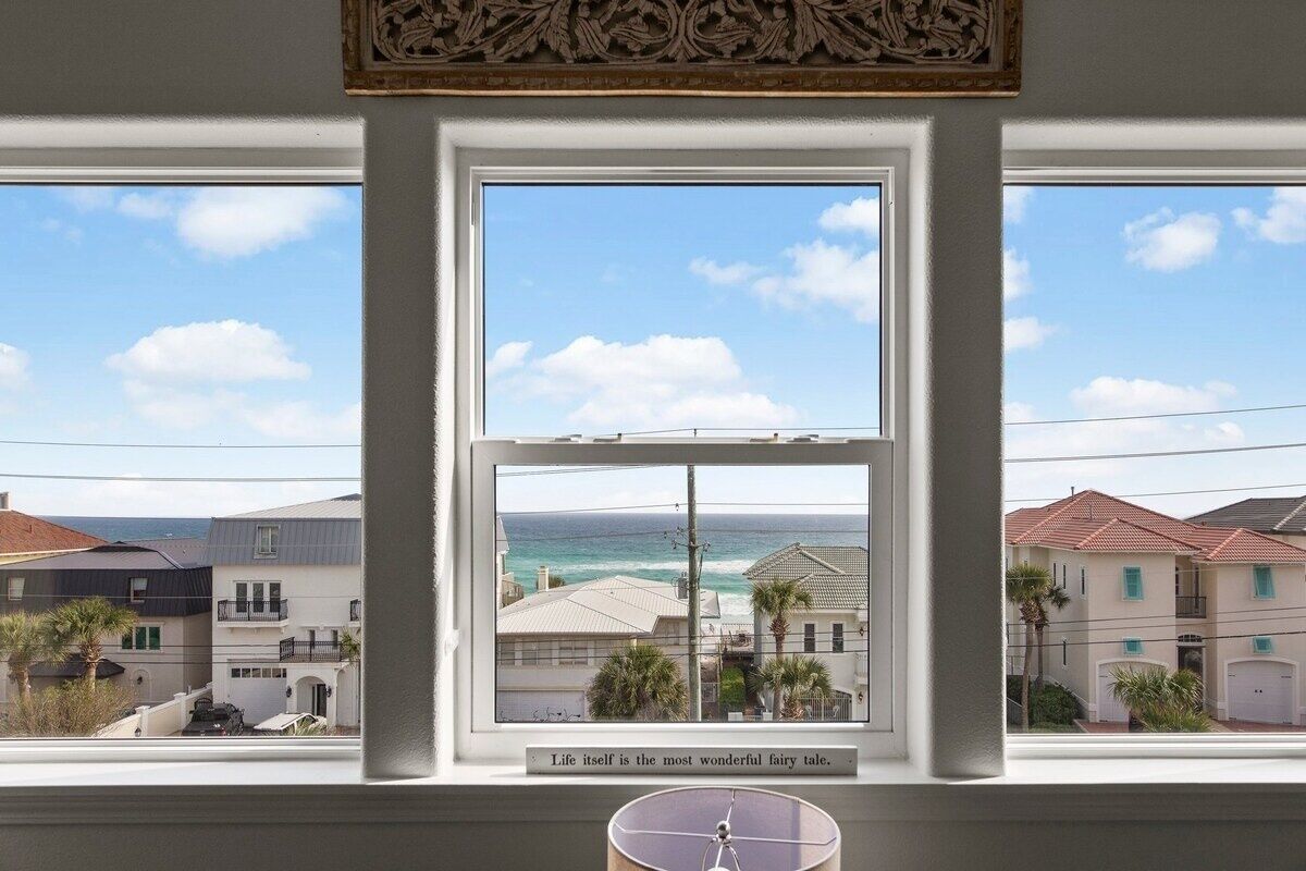 Ein Zimmer mit großem Fenster und Blick auf eine Küstenlandschaft, inklusive Meer und umliegende Gebäude.