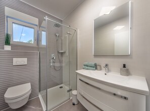 Ein modernes Badezimmer mit einer Duschkabine, einer Toilette, einem Waschbecken mit Spiegel und einem Fenster über der Toilette.