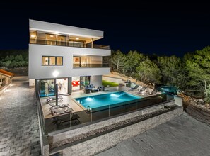Ein modernes, zweistöckiges Haus mit Swimmingpool, Sitzgelegenheit im Freien und Blick auf Bäume.