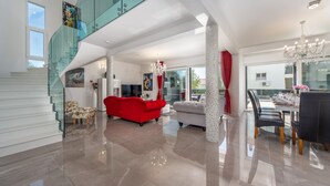 A spacious living area with a red sofa, a dining table set for six, and a staircase with glass railings. - Villa Shaula (Sibenik)