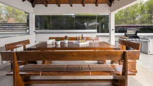 A spacious outdoor dining area with a wooden table and benches, large windows, and a barbecue grill. - Villa Shaula (Sibenik)