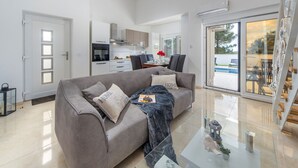 A modern living room with a grey sofa, a glass coffee table, and a kitchen in the background.