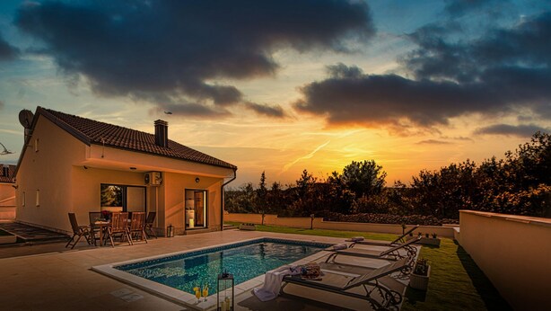A modern house with a swimming pool, patio furniture, and a view of the sunset.