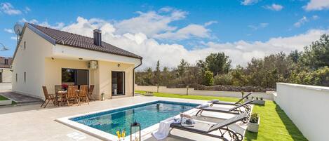 A modern house with a swimming pool, outdoor seating, and a well-maintained lawn.