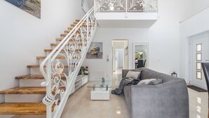 A modern living room with a staircase, a grey sofa, and a glass coffee table.