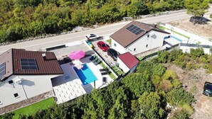 A residential property with a swimming pool, solar panels, and a red car parked outside.