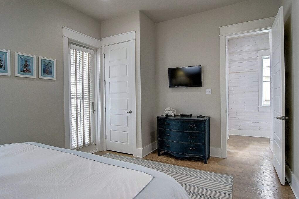 Une chambre à coucher avec un lit, une commode, un téléviseur fixé au mur et deux portes.