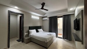 A modern hotel room with a bed, bedside tables, a ceiling fan, an air conditioning unit, and a TV mounted on the wall. - Aster Studio Serviced Apartment (Gurugram)