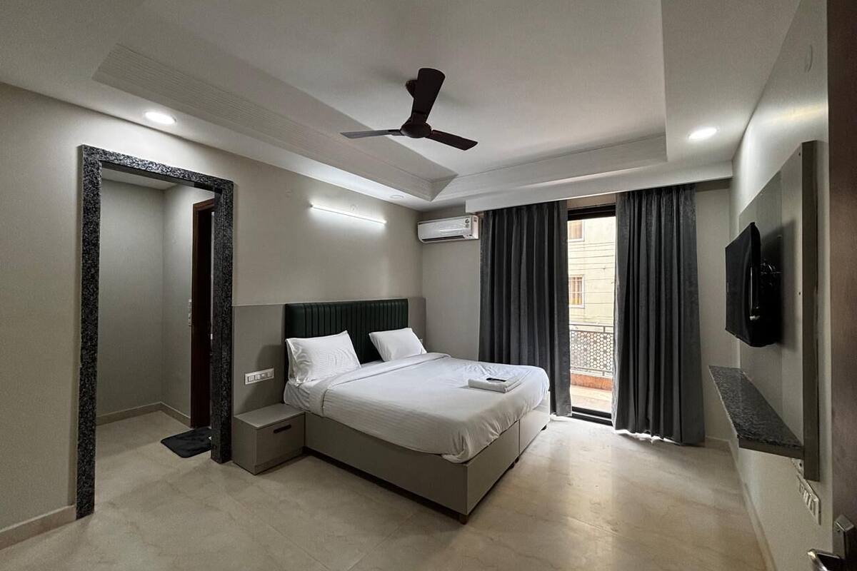 Ein modernes Hotelzimmer mit einem Bett, Nachttischen, einem Deckenventilator, einer Klimaanlage und einem an der Wand befestigten Fernseher.