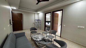 A modern living room with a sofa, a dining table, and chairs. There is a ceiling fan and a door leading to another room. - Aster Studio Serviced Apartment (Gurugram)
