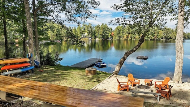 Un área de estar al aire libre frente al lago, con una mesa y sillas de madera, rodeada de árboles y vistas al lago.