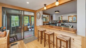 Una cocina moderna con vigas de madera, una barra con taburetes y un ventanal corredero que da a un comedor.
