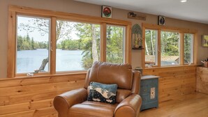 Una habitación con un sillón de cuero, paredes de madera y ventanas amplias con vista a un lago.