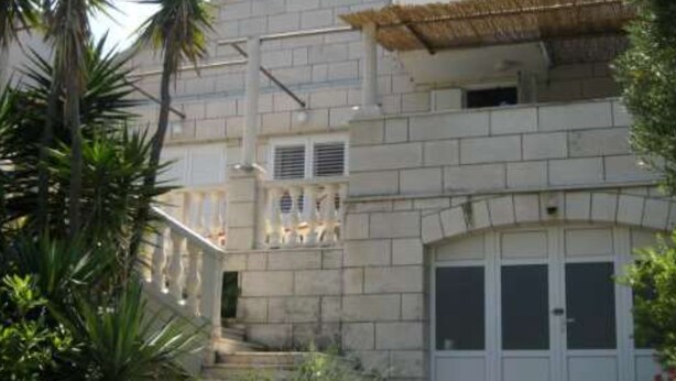 A building with a stone facade, a balcony with railings, and a covered area with a thatched roof. - Apartment Jadranka (Lumbarda)