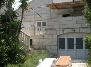 Un edificio con fachada de piedra, un balcón con barandilla y una zona cubierta con tejado de paja.