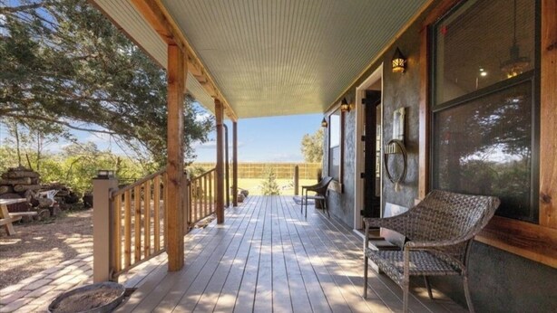 A wooden deck with a railing, a wicker chair, and a view of a natural landscape.