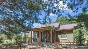 A rustic cabin with a porch, a wooden fence, and a wheelbarrow.