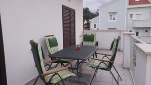En balkong med ett bord och fyra stolar, en dörr och ett räcke.