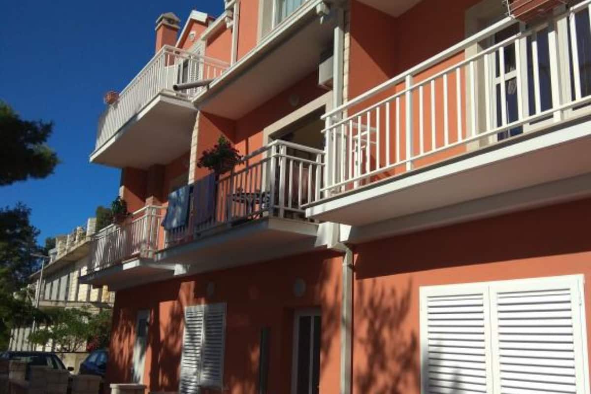 A multi-story building with balconies, shutters, and a clear blue sky.
