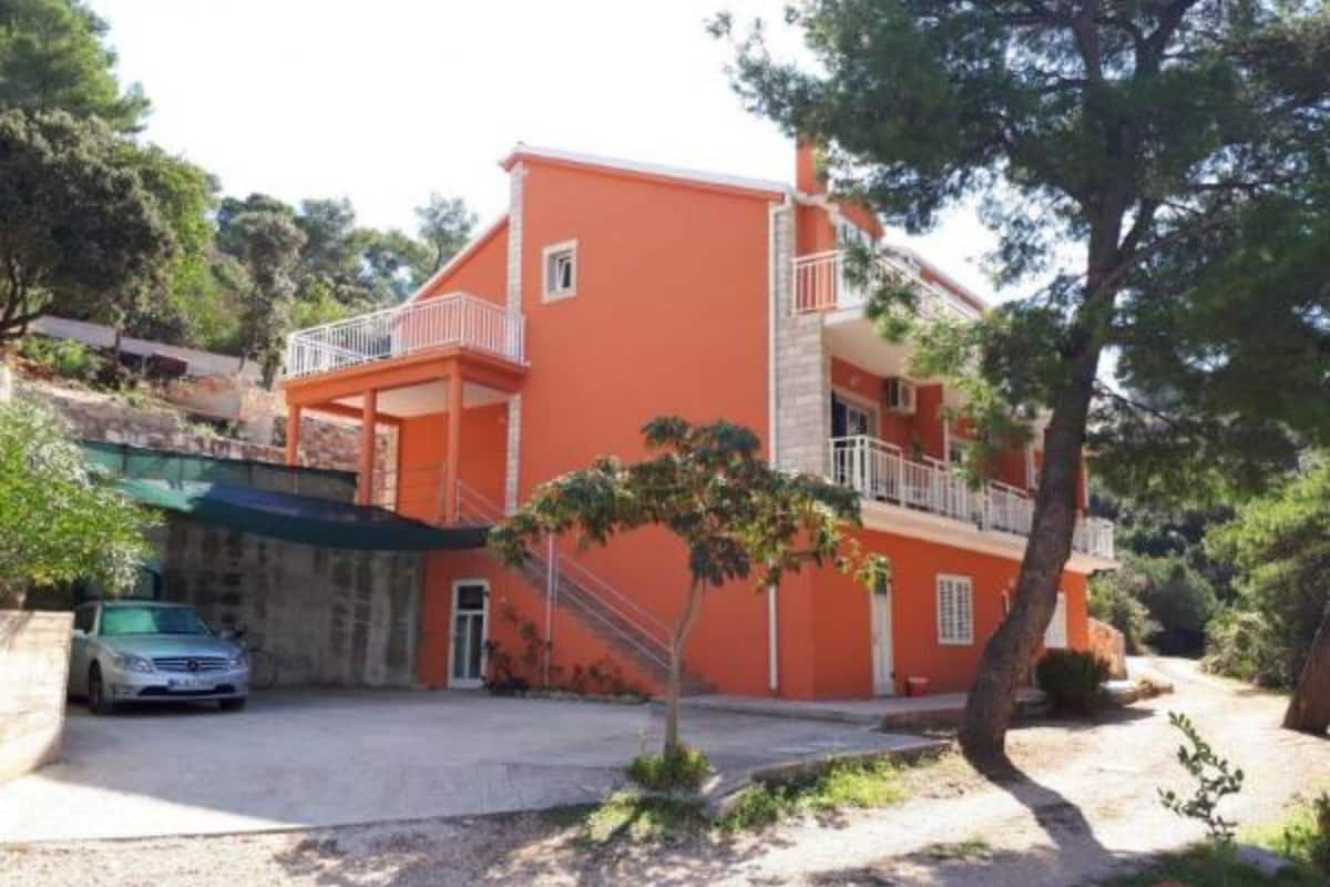 A two-story building with a red exterior, a balcony on the upper floor, and a car parked in front.