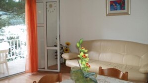 A living room with a beige sofa, a dining table with a lace tablecloth, and a potted plant.