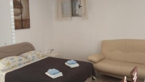 A bedroom with a bed, a sofa, a window with curtains, and a wall-mounted artwork.