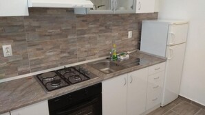 A kitchen with a gas stove, dishwasher, white cabinets, and a refrigerator.