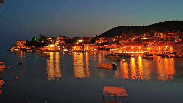 A coastal town at dusk with illuminated buildings and boats on the water.