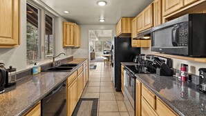 A modern kitchen with granite countertops, wooden cabinets, a stainless steel refrigerator, and a built-in microwave.