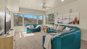 A spacious living room with teal sofas, a flat-screen TV, and large windows offering a mountain view.