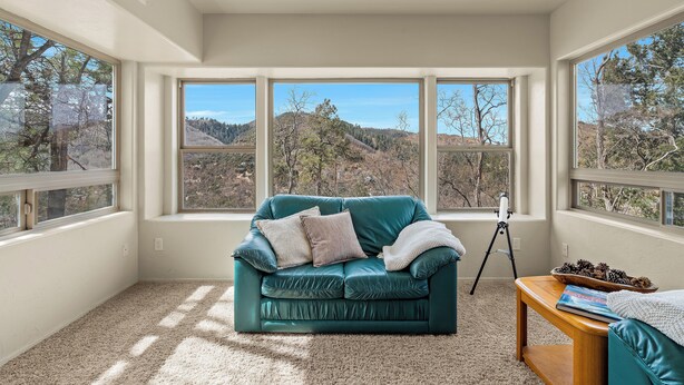 A room with a teal leather sofa, a wooden side table, and a large window with a mountain view.