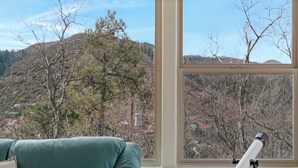 A telescope on a tripod by a window with a view of a mountainous landscape.