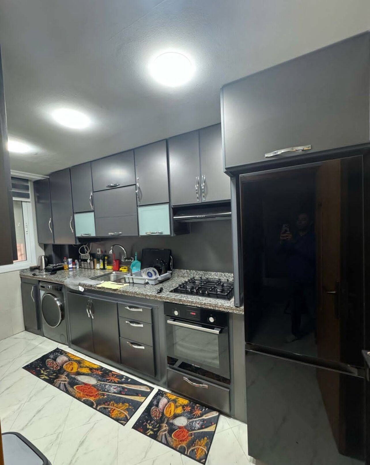 A modern kitchen with dark cabinets, a gas stove, a built-in oven, and a refrigerator.