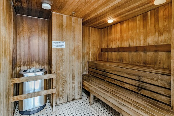 Una sauna seca con bancos de madera y un recipiente metálico para agua.