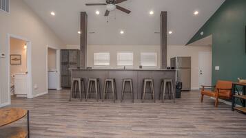 A spacious living area with a central kitchen island, a ceiling fan, and a dining area with stools.