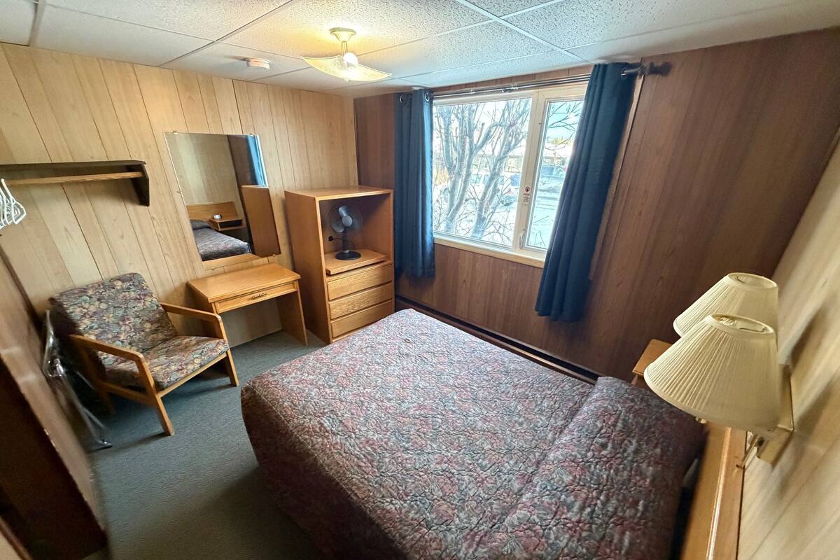 Una stanza arredata con un letto, una scrivania, una sedia, un comò, uno specchio e una finestra con tende.