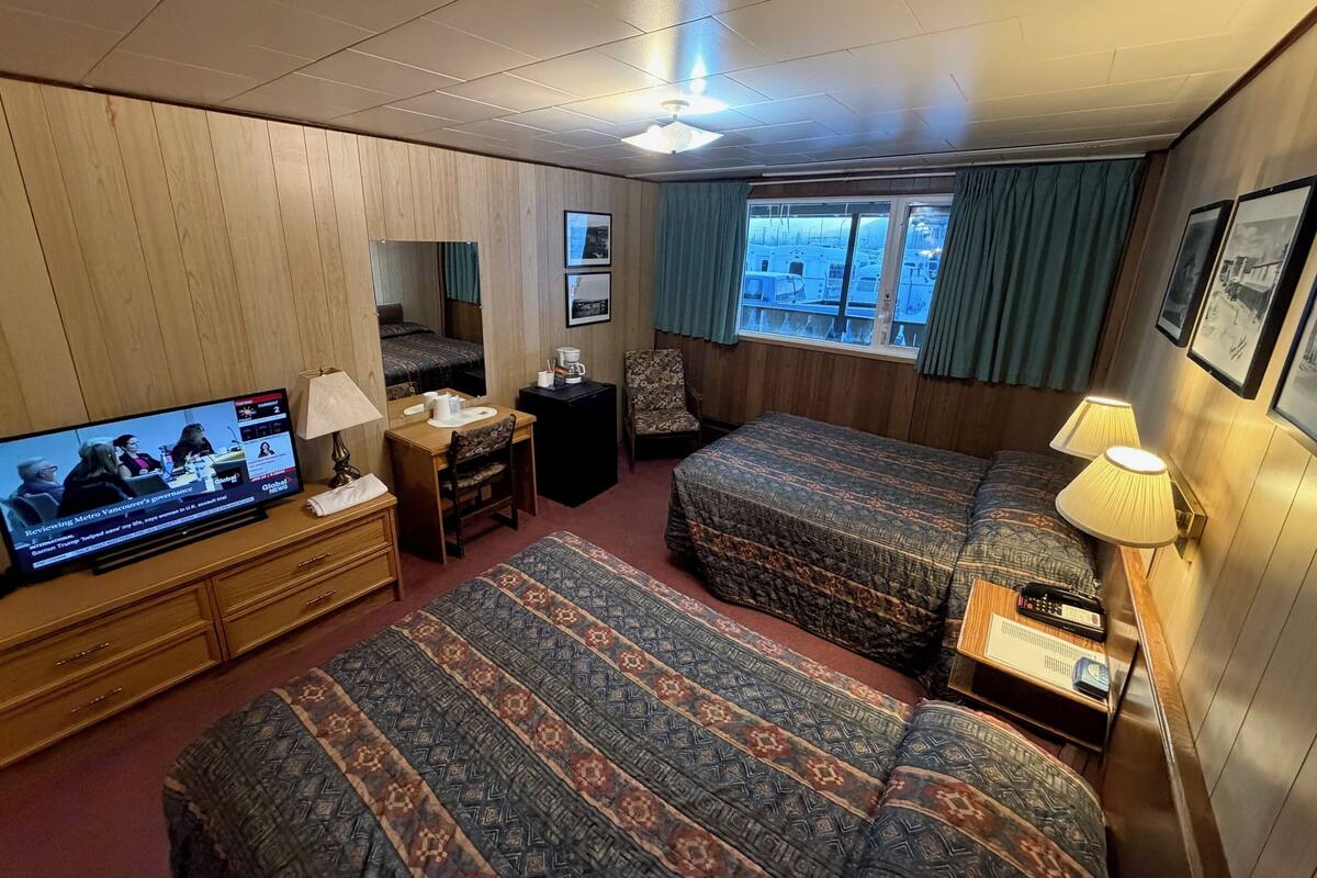 Una camera d'albergo con due letti, una scrivania con televisore, una sedia e una finestra con tende.