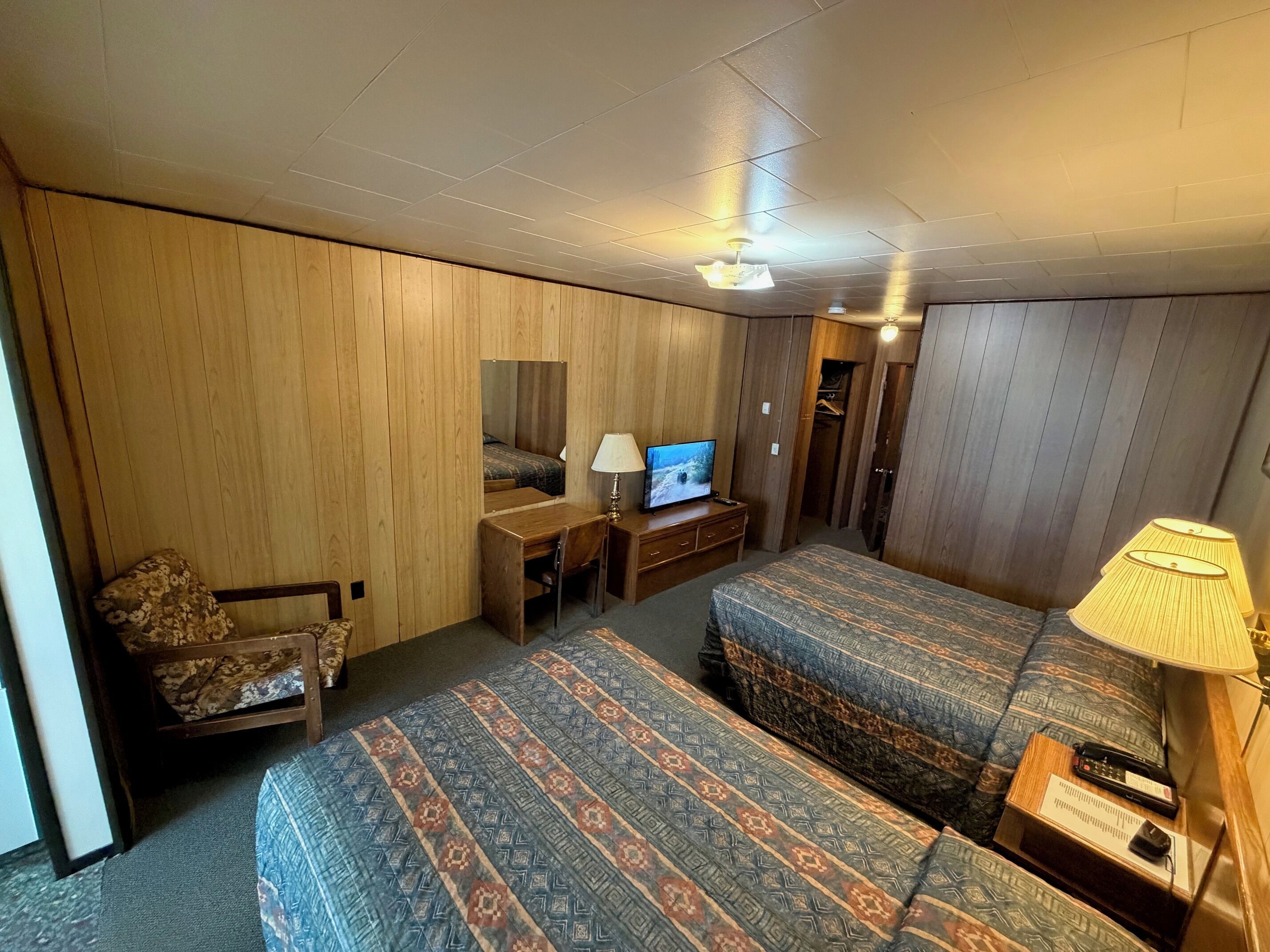 Ein kleines Hotelzimmer mit zwei Einzelbetten, einem kleinen Schreibtisch, einem Fernseher, einem Stuhl und einer Lampe.