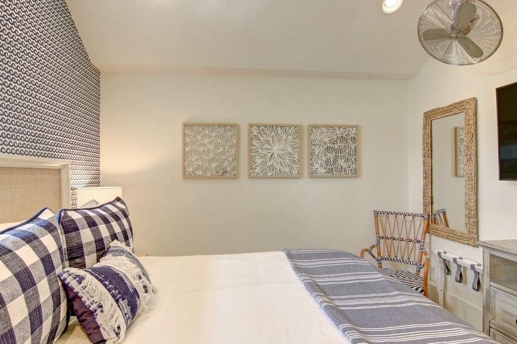 Une chambre à coucher avec un lit, des oreillers, une chaise, un miroir et des œuvres d’art murales.