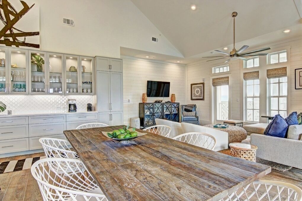 A spacious kitchen with white cabinetry, a wooden dining table, and a large window.