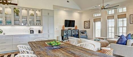 A spacious kitchen with white cabinetry, a wooden dining table, and a large window.