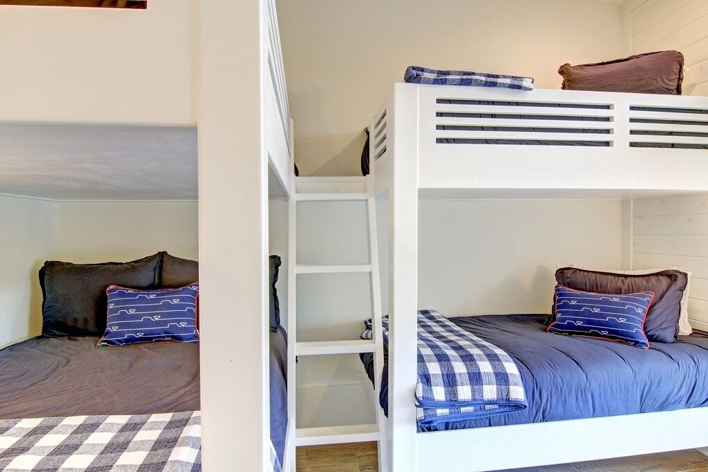 Une chambre avec un lit superposé, une couette à carreaux, des oreillers et une échelle blanche.
