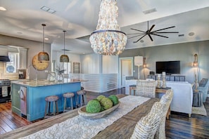 A spacious living area with a central island, bar stools, a chandelier, and a television in the background. - Shore Beats Workin' 216 BE (Port Aransas)