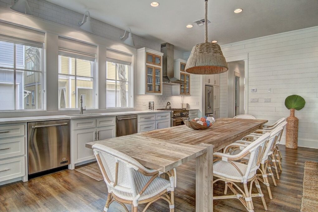 A spacious kitchen with a long island, white cabinetry, stainless steel appliances, and a hanging light fixture.