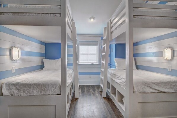 A narrow hallway with bunk beds on either side, a window at the end, and a door with a light fixture. - Shore Perfection 118 CE (Port Aransas)