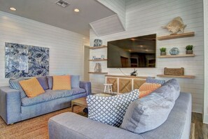 A modern living room with two sofas, a coffee table, and a TV mounted on the wall. There are shelves with decorative items and a large abstract painting on the wall. - Shore Perfection 118 CE (Port Aransas)